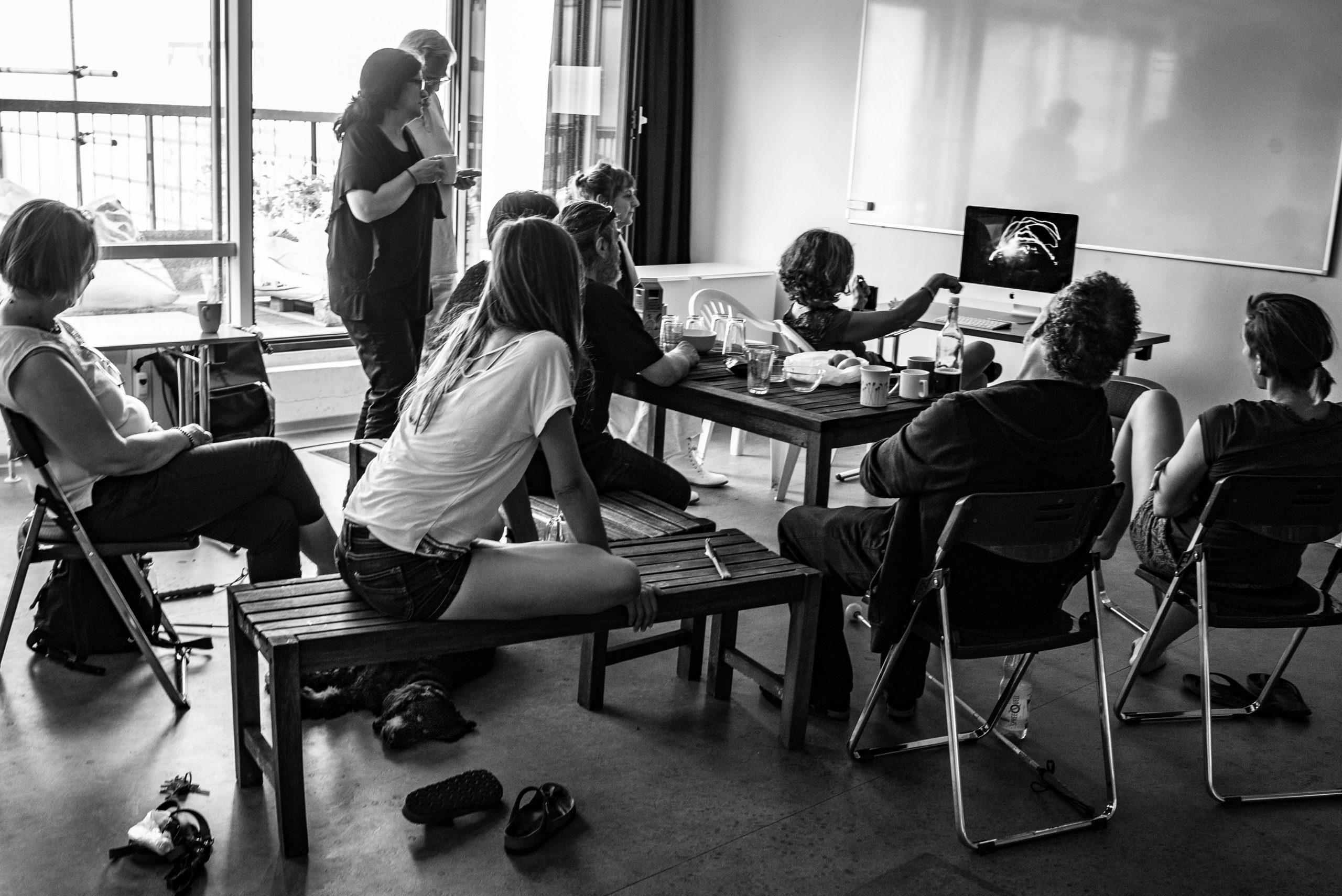 Bildbesprechungsrunde im Fotostudio für Blinde Fotografen © Karsten Hein Eine Gruppe sommerlich gekleideter Menschen, die teils sitzend, teils stehend voller Interesse auf einen Bildschirm schauen.